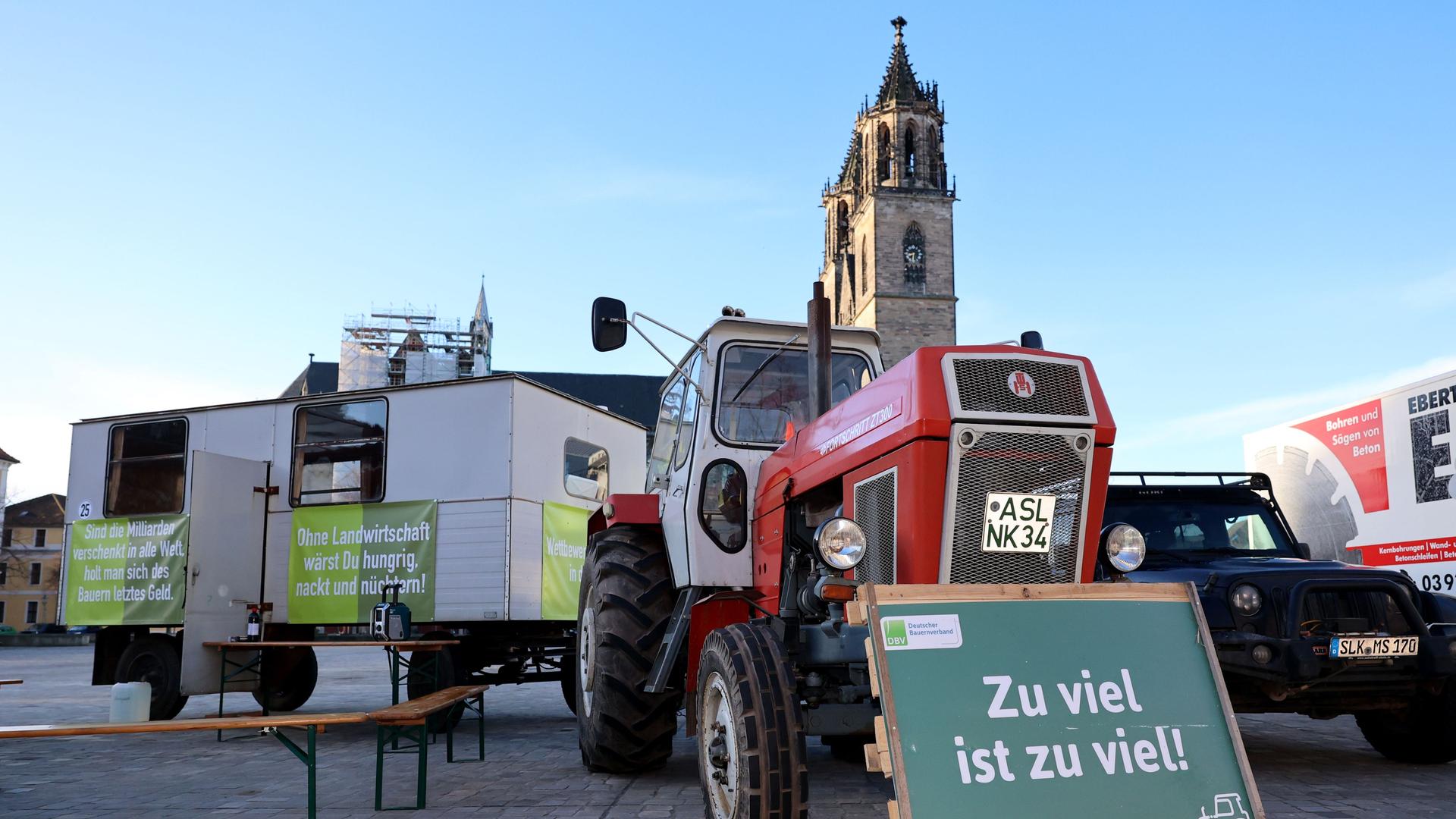 Ein Plakat «Zu viel ist zu viel!» steht vor einem Traktor, während einer Mahnwache von Landwirten auf dem Domplatz von Magdeburg.
