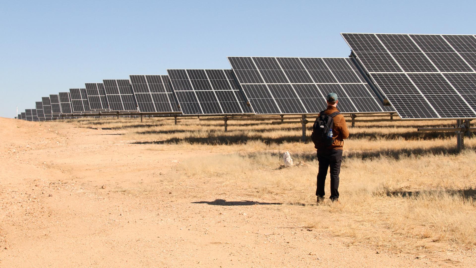 Ein Mann steht vor einer Photovoltaikanlage mitten in der namibischen Steppe. 