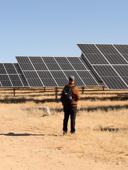 Ein Mann steht vor einer Photovoltaikanlage mitten in der namibischen Steppe. 