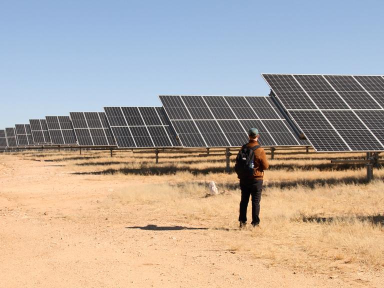 Ein Mann steht vor einer Photovoltaikanlage mitten in der namibischen Steppe. 