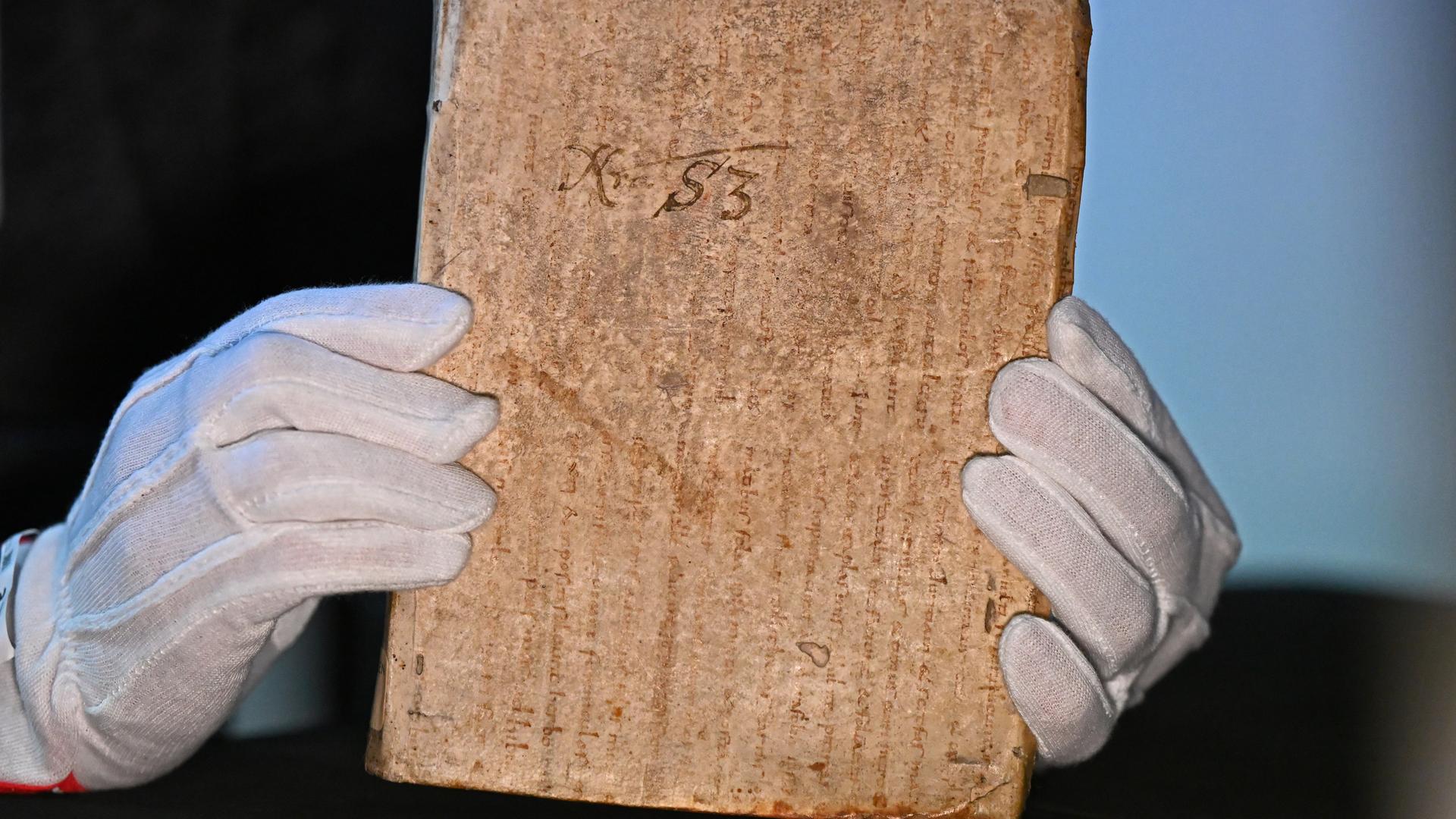 Ein Mann hält mit Handschuhen ein sehr altes Papier.