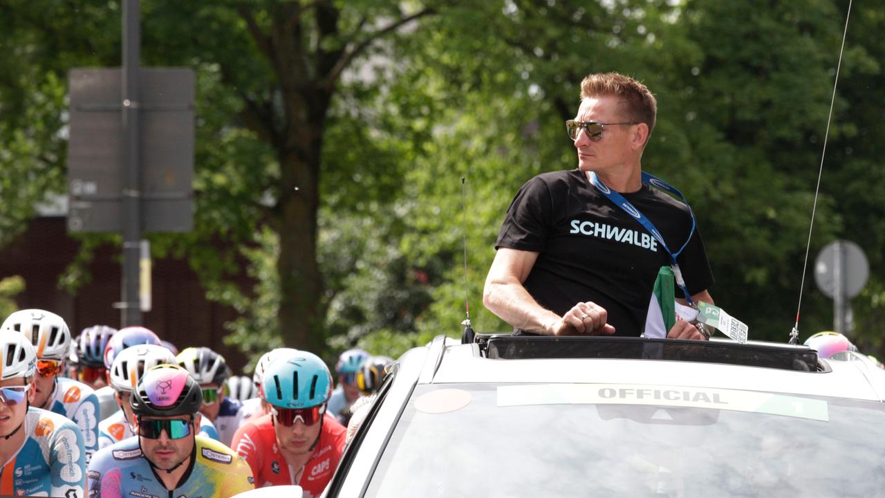 Der Ex-Radsportprofi André Greipel schaut aus dem Dachfenster eines fahrenden Autos auf Radprofis um ihn herum