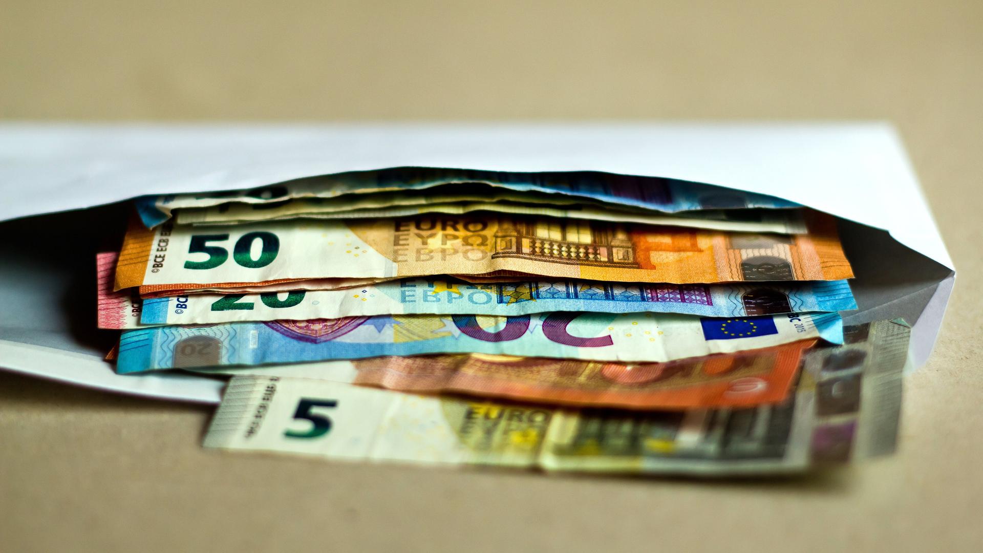 Mehrere unterschiedliche Euro-Geldscheine liegen in einem offenen Briefumschlag auf einem Tisch.