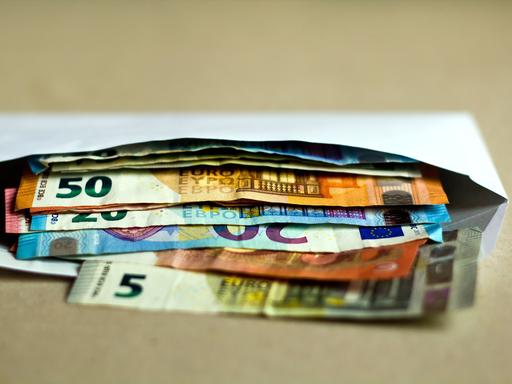 Mehrere unterschiedliche Euro-Geldscheine liegen in einem offenen Briefumschlag auf einem Tisch.