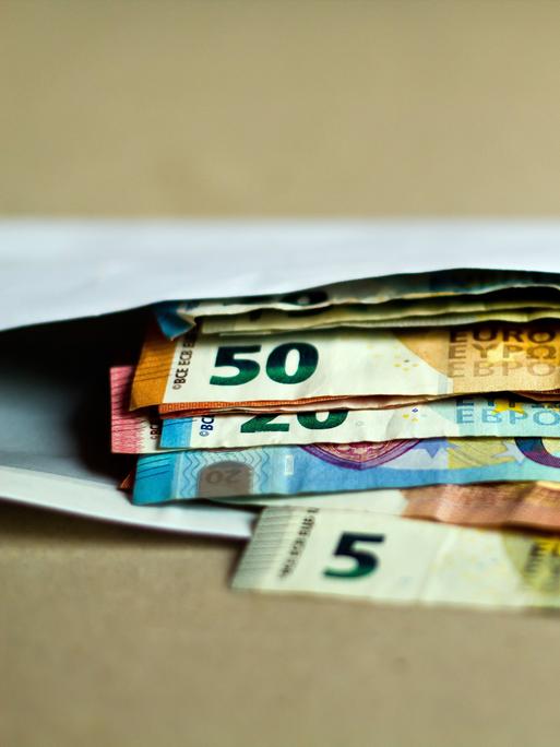 Mehrere unterschiedliche Euro-Geldscheine liegen in einem offenen Briefumschlag auf einem Tisch.
