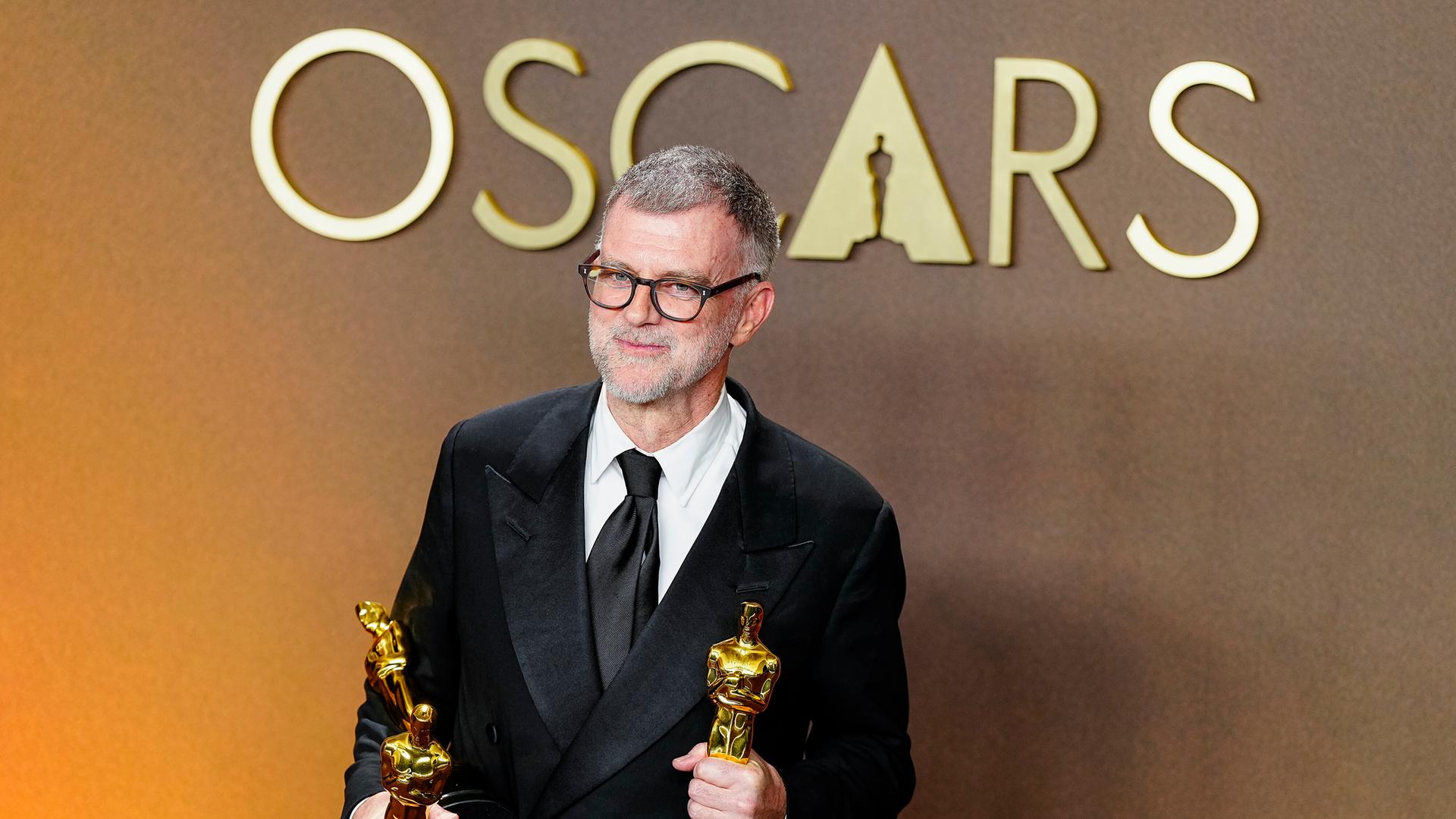 Paul Thomas Anderson, Regisseur des Politthrillers "One Battle After Another" schaut in die Kamera. Er hält zwei der insgesamt sechs Oscars, die der FIlm gewonnen hat, in den Händen.