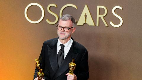 Paul Thomas Anderson, Regisseur des Politthrillers "One Battle After Another" schaut in die Kamera. Er hält zwei der insgesamt sechs Oscars, die der FIlm gewonnen hat, in den Händen.