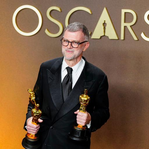 Paul Thomas Anderson, Regisseur des Politthrillers "One Battle After Another" schaut in die Kamera. Er hält zwei der insgesamt sechs Oscars, die der FIlm gewonnen hat, in den Händen.