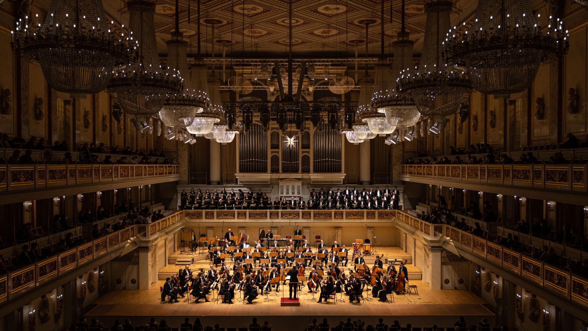 Blick auf die Bühne des Konzerthauses, auf dem ein Orchester auf der Bühne zu sehen und dazu ein Chor auf der darüber liegenden Empore.