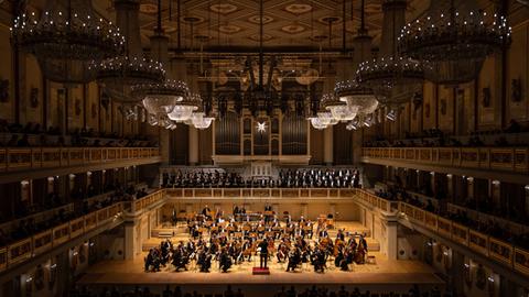 Blick auf die Bühne des Konzerthauses, auf dem ein Orchester auf der Bühne zu sehen und dazu ein Chor auf der darüber liegenden Empore.