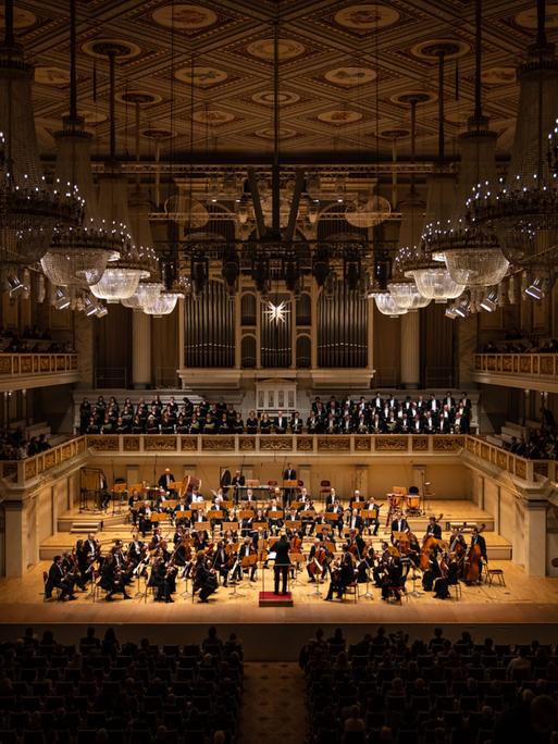 Blick auf die Bühne des Konzerthauses, auf dem ein Orchester auf der Bühne zu sehen und dazu ein Chor auf der darüber liegenden Empore.