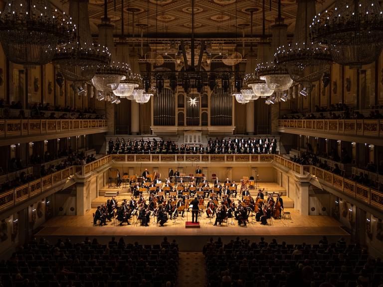 Blick auf die Bühne des Konzerthauses, auf dem ein Orchester auf der Bühne zu sehen und dazu ein Chor auf der darüber liegenden Empore.