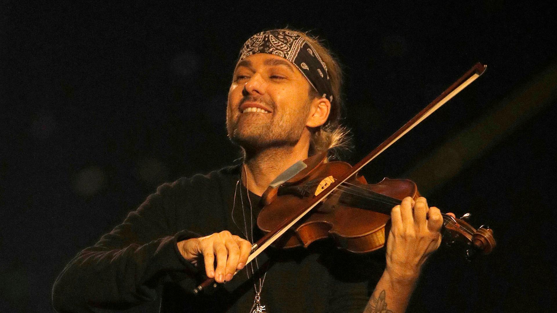 David Garrett spielt Geige. Er trägt Dreitagebart und hat ein Stirnband an, die Haare hat er zum Zopg zusammengebunden. David Garrett spielt Geige. Er trägt Dreitagebart und hat ein Stirnband an, die Haare hat er zum Zopg zusammengebunden.