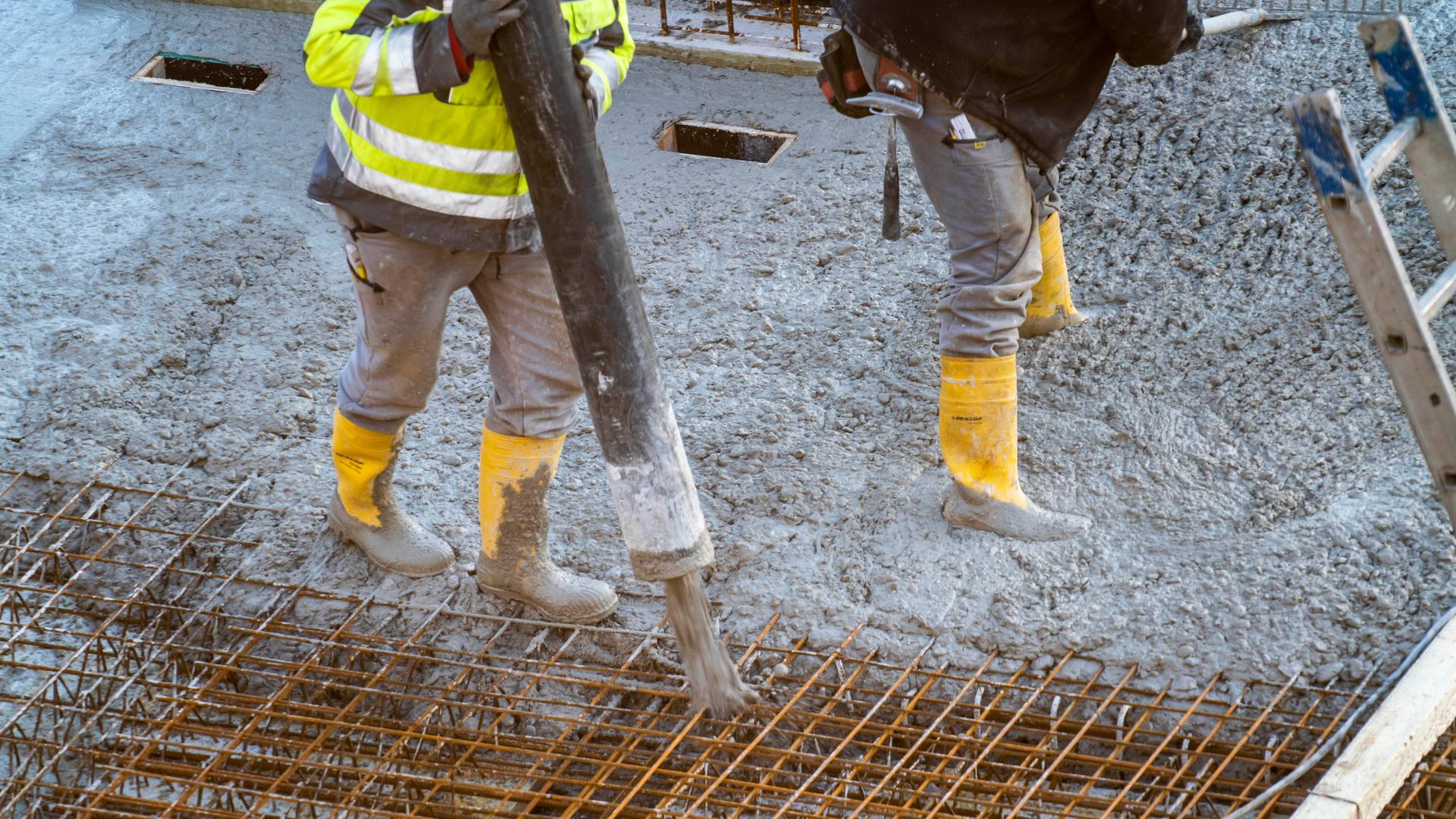 Auf einer Baustelle eines Gebäudes wird von Bauarbeitern Beton per Betonpumpe aufgetragen.