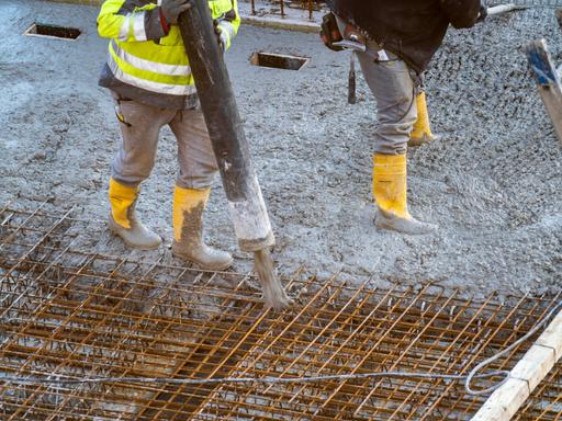 Auf einer Baustelle eines Gebäudes wird von Bauarbeitern Beton per Betonpumpe aufgetragen.