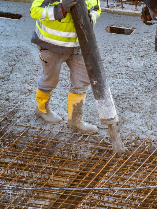 Auf einer Baustelle eines Gebäudes wird von Bauarbeitern Beton per Betonpumpe aufgetragen.
