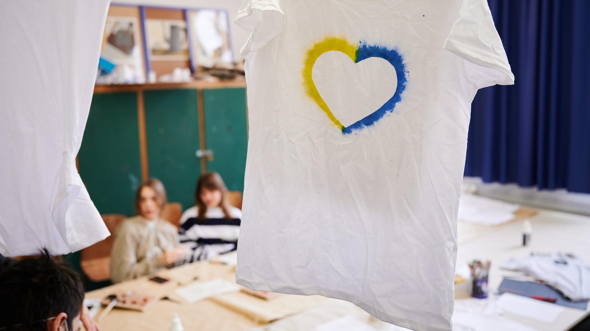 Ein T-Shirt mit einem Herz, umrahmt von den ukrainischen Farben hängt im Klassenraum einer Willkommensklasse am Willy-Graf-Gymnasium in Berlin-Lichterfelde. 