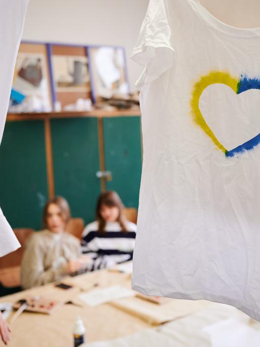 Ein T-Shirt mit einem Herz, umrahmt von den ukrainischen Farben hängt im Klassenraum einer Willkommensklasse am Willy-Graf-Gymnasium in Berlin-Lichterfelde. 