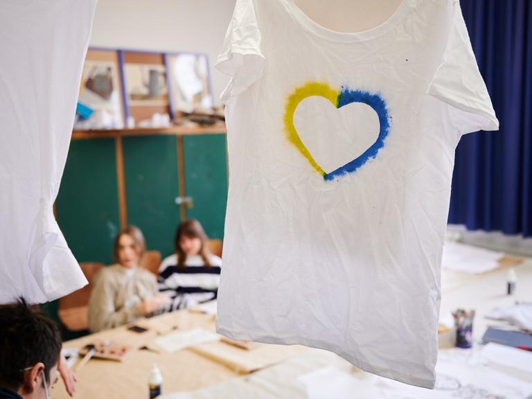 Ein T-Shirt mit einem Herz, umrahmt von den ukrainischen Farben hängt im Klassenraum einer Willkommensklasse am Willy-Graf-Gymnasium in Berlin-Lichterfelde. 