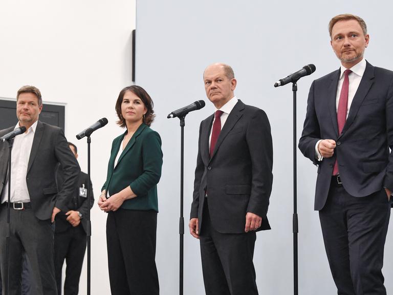 Robert Habeck, Annalena Baerbock, Olaf Scholz und Christian Lindner stehen während einer Pressekonferenz am Mikrofon.