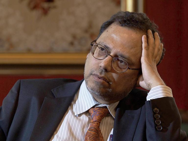 Der bengalische Philosoph Dipesh Chakrabarty bei einem Interview. Er hält den Kopf leicht geneigt und schaut nachdenklich. Seine linke Hand stützt seinen Kopf.