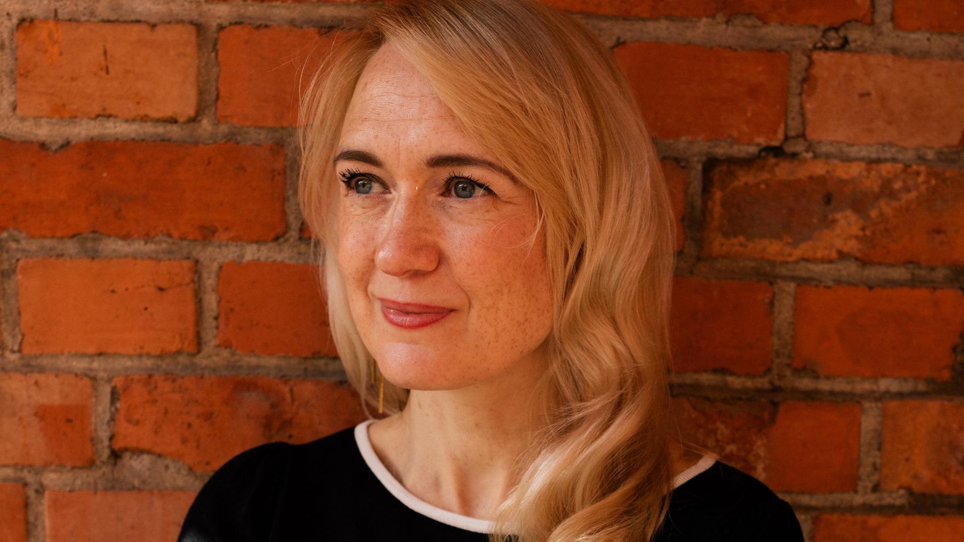 Schriftstellerin Anousch Mueller steht lächelnd vor einer Backsteinmauer.