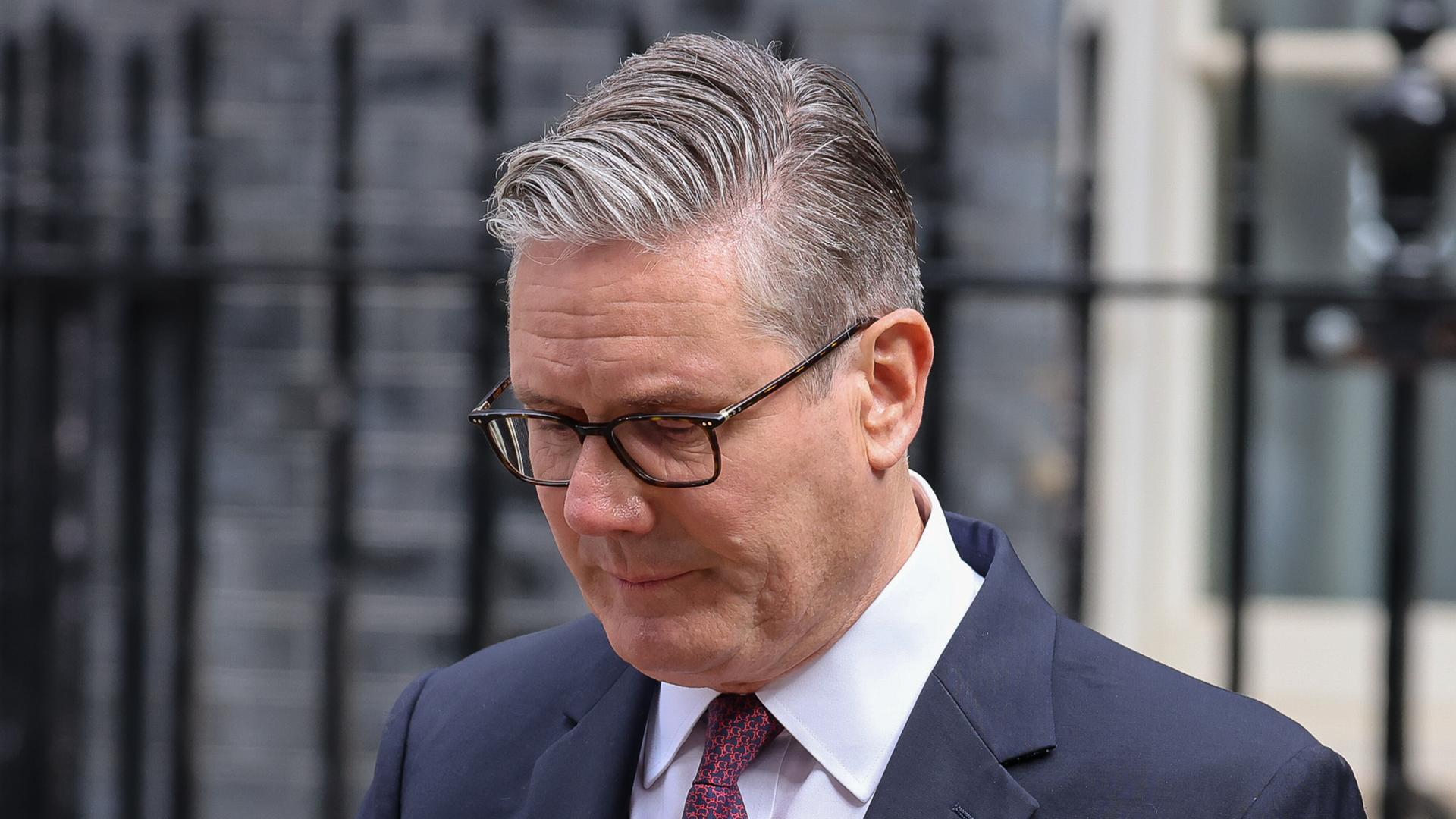 Keir Starmer steht im Anzug mit gesenktem Blick vor einem Metallzaun Keir Starmer steht im Anzug mit gesenktem Blick vor einem Metallzaun