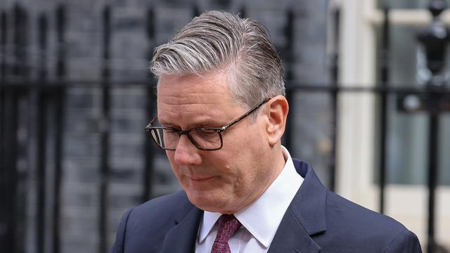Keir Starmer steht im Anzug mit gesenktem Blick vor einem Metall-Zaun