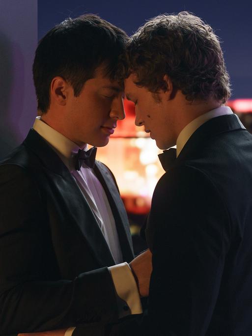Zwei Männer im Anzug sind sich sehr nahe; sie lehnen ihre Köpfe aneinander und berühren sich.