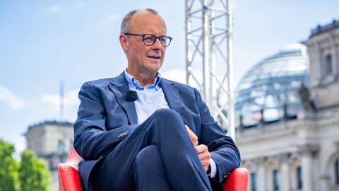 CDU-Vorsitzender Friedrich Merz sitzt im ARD-Sommerinterview auf einem roten Sessel, im Hintergrund ist die Kuppel des Berliner Reichstagsgebäudes zu sehen