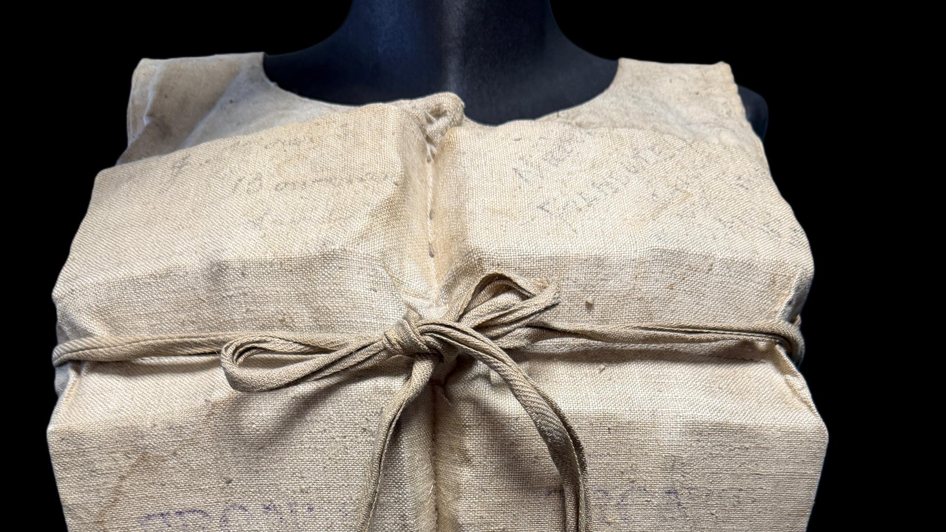 Eine alte Rettungsweste der Titanic. Der Bezug ist beige und die Weste ist vorne geschnürt.