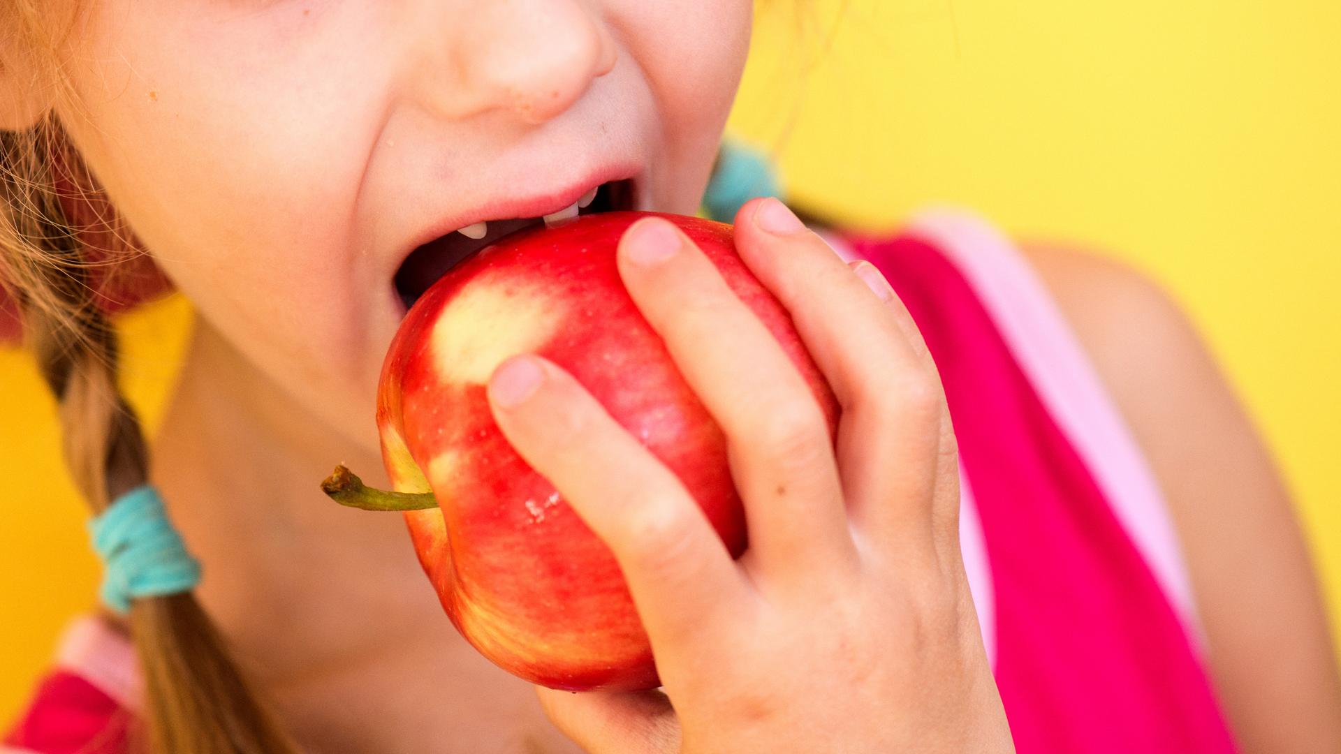 Ein Mädchen mit Zahnlücke beißt herzhaft in einen Apfel.