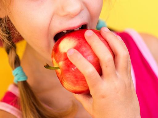 Ein Mädchen mit Zahnlücke beißt herzhaft in einen Apfel.