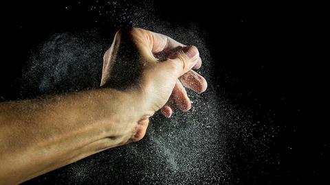 Eine Bäckerhand stiebt Mehl in seine Umgebung.