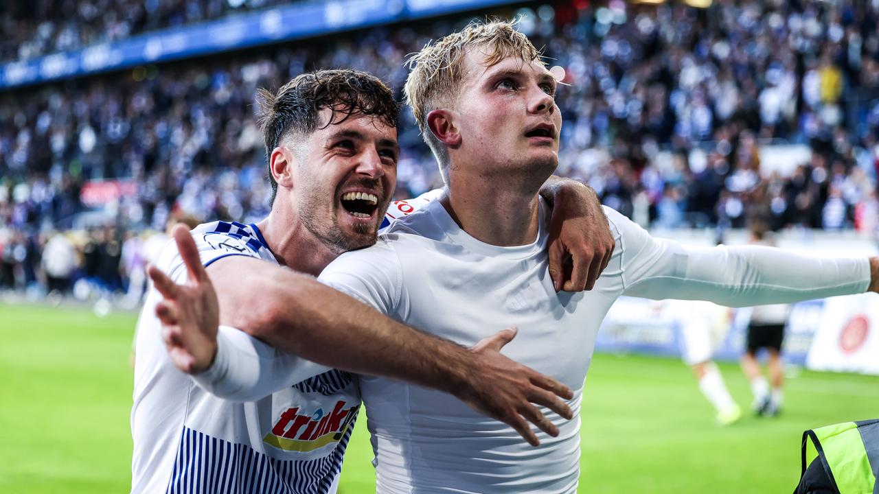 Remmert in weißem Unterziehshirt und ohne Trikot, breitet zum Torjubel die Arme aus und wird von hinten vom lachenden Mitspieler Tobias Fleckstein umarmt.