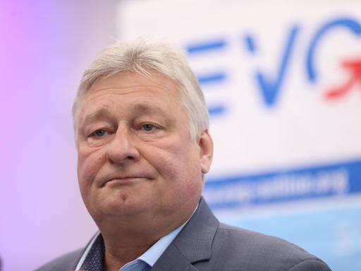 Der Vorsitzende der Eisenbahn- und Verkehrsgewerkschaft (EVG), Martin Burkert schaut kritisch, im Hintergrund eine hellblaue Wand mit dem Schriftzug der Gewerkschaft. 