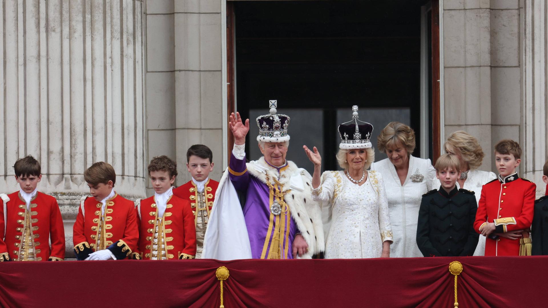 Charles und Kamilla stehen auf dem Balkon des Buckingham Palace und winken.