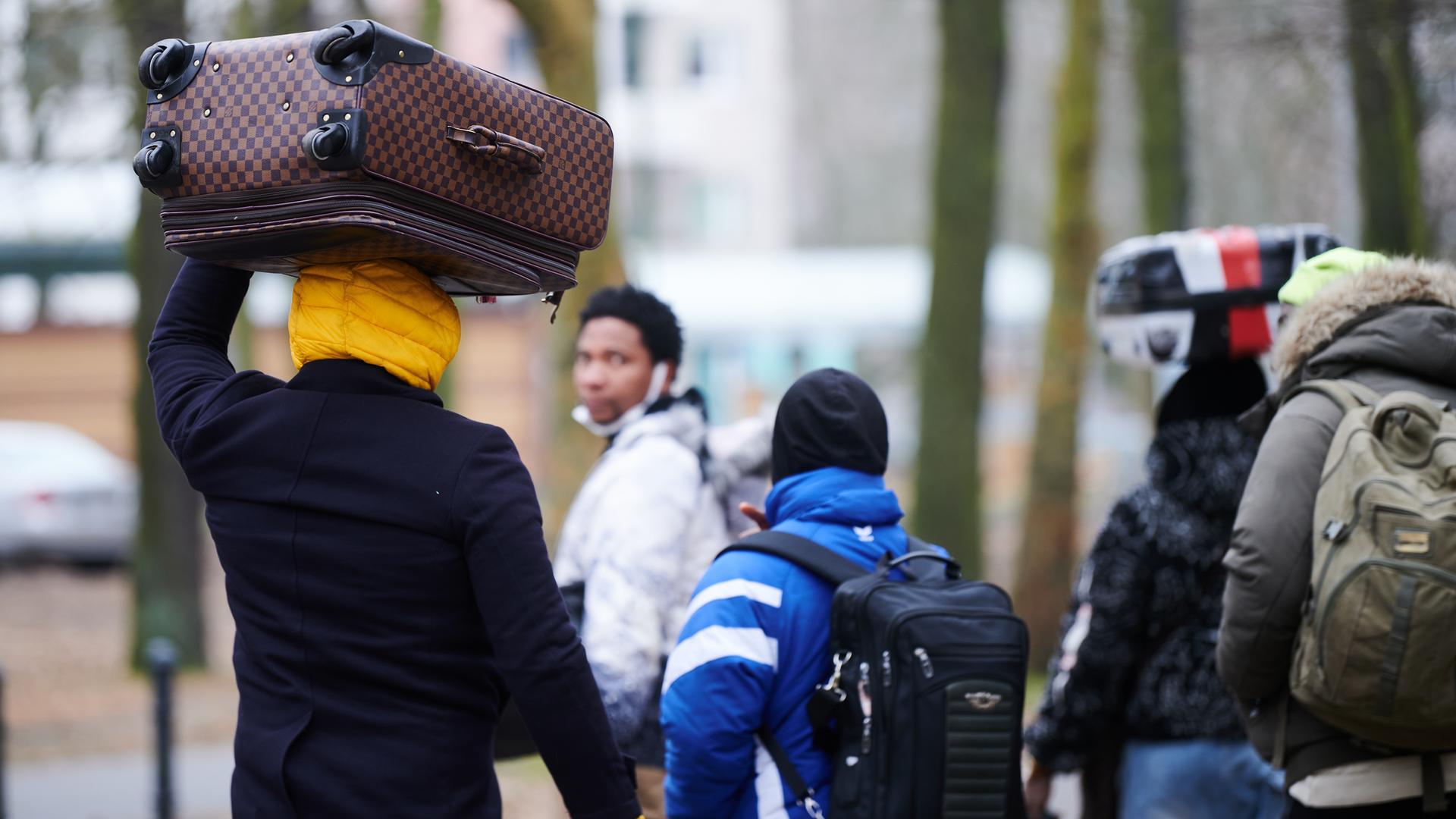 Fünf Flüchtlinge tragen ihre Koffer auf dem Kopf, während sie in ein Ankunftszentrum gehen. (Symbolbild)