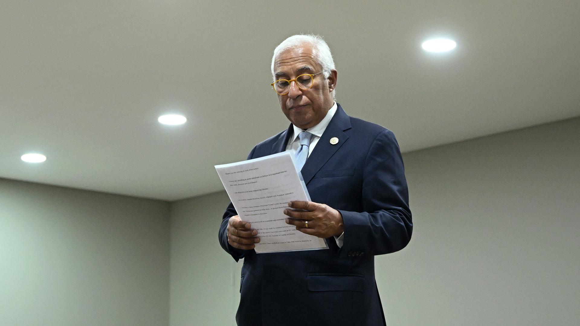 Costa steht in einem Raum und blickt in ein Manuskript, das er in den Händen hält