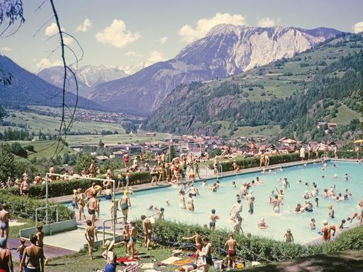 Gut gefülltes Schwimmbad vor der Kulisse der Alpen an einem sonnigen Sommertag Ötz in Österreich. Historische, kolorierte Postkarte.