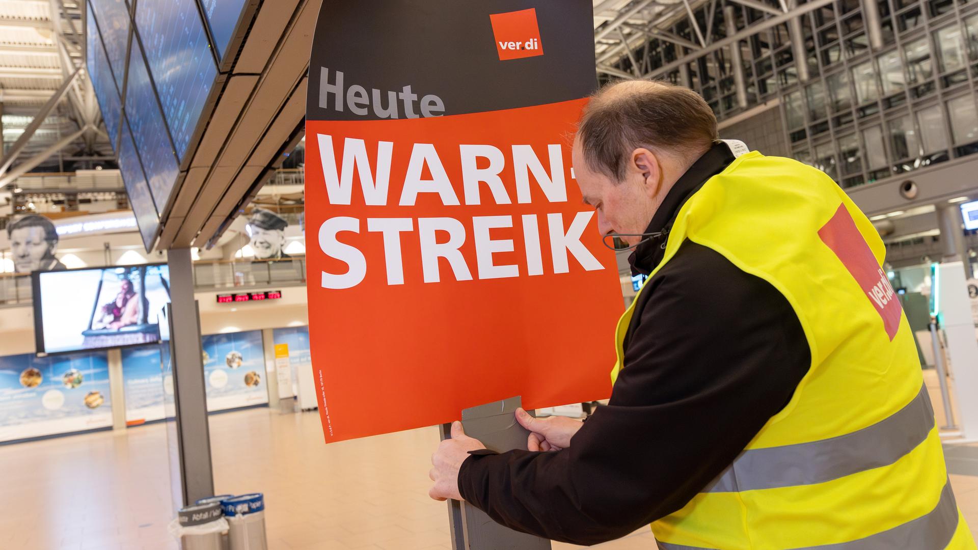 Ein Verdi-Vertreter hängt ein Plakat mit der Aufschrift "Warnstreik" in einem Terminal im Hamburger Flughafen auf. 