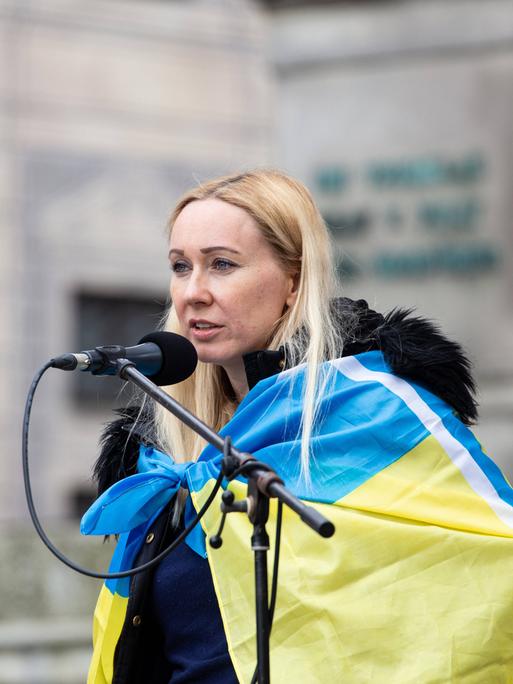 Daria Onyshchenko am Mikrofon mit Ukraine-Flagge um die Schultern.