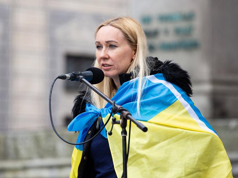 Daria Onyshchenko am Mikrofon mit Ukraine-Flagge um die Schultern.