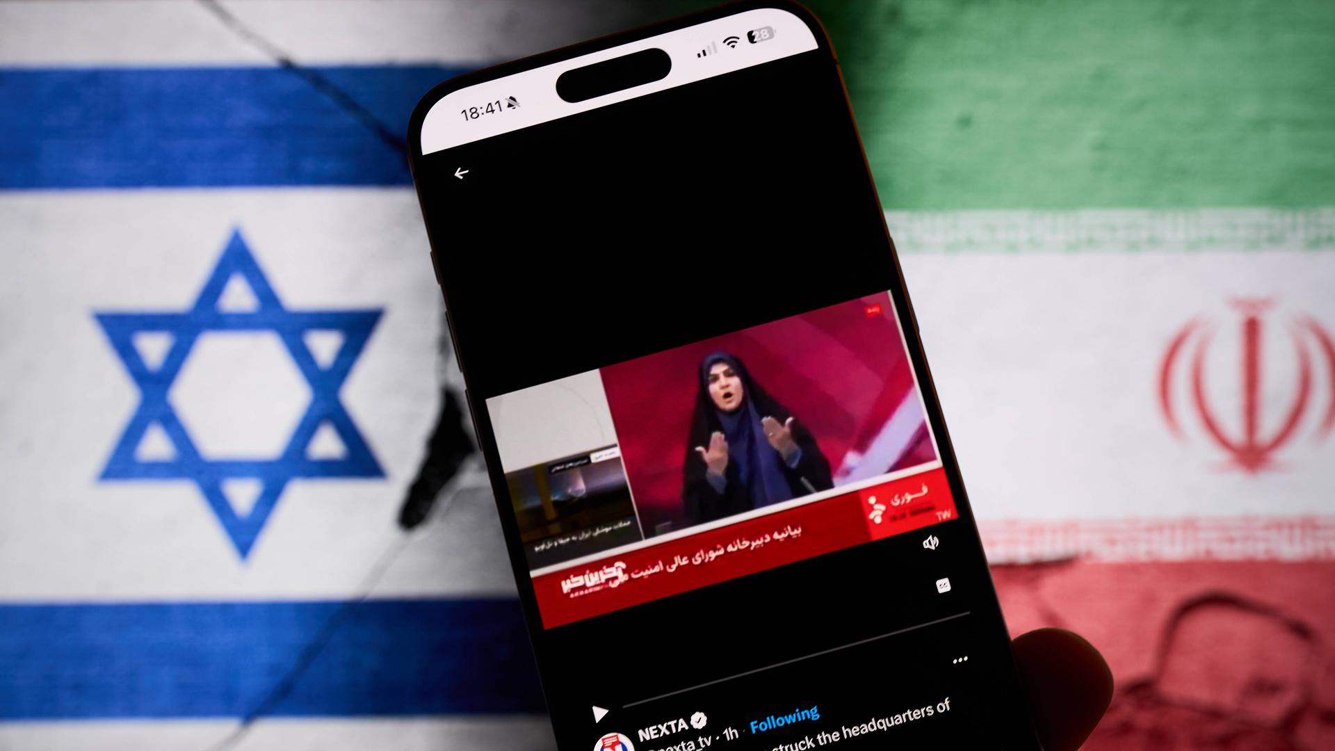 Fotomontage: Im Hintergrund die iranische und die israelische Flagge. Im Vordergrund ein Mobiltelefon: darauf abgebildet ist die Moderatorin des staatlichen Fernsehens im Iran vor einem israelischen Angriff.