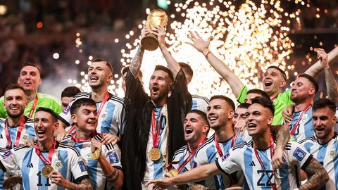 Kapitän Lionel Messi reckt bei der Siegesfeier mit der argentinischen Mannschaft den goldenen Pokal im Lusail Iconic Stadium nach oben