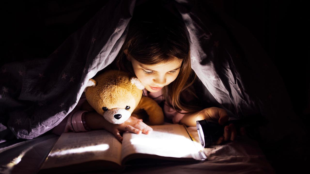 Kind, das ein Buch unter einer Decke mit einem Teddybär liest, beleuchtet von Taschenlampe. Kind, das ein Buch unter einer Decke mit einem Teddybär liest, beleuchtet von Taschenlampe.