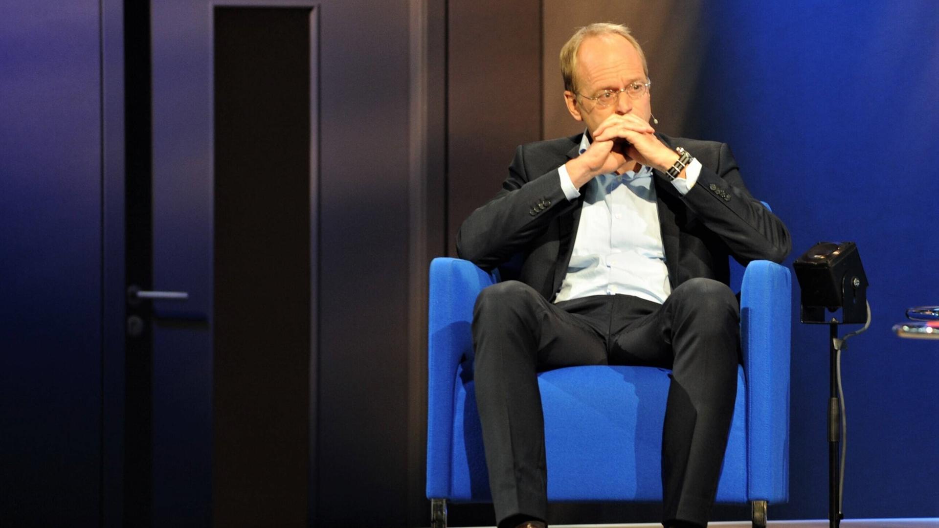 Klaus Zierer sitzt auf einer Bühne in einem Sessel, er hält die Hände vor dem Mund verschränkt. Klaus Zierer sitzt auf einer Bühne in einem Sessel, er hält die Hände vor dem Mund verschränkt.