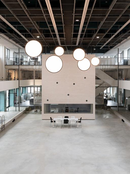 Blick in eine ehemalige Schwimmhalle: im leeren Becken ein quaderförmiger Pavillon, von der Decke hängt eine Installation mit kreisförmigen, leuchtend weißen Scheiben.