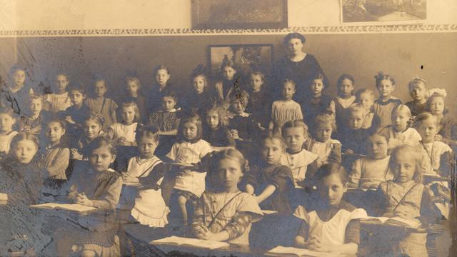 Gruppenaufnahme einer Schulklasse um 1910: Eine Lehrerin steht inmitten der Mädchenklasse