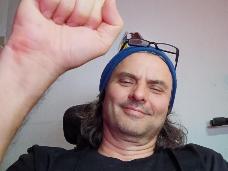Michael Kobs trägt ein T-Shirt, auf dem "Truth" steht. Er streckt seine Fuß zum solidarischen Gruß in die Kamera.